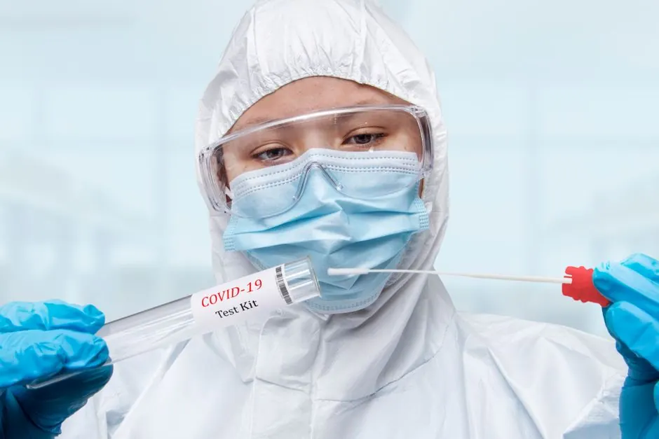 Close-up of a healthcare worker in PPE preparing a COVID-19 test kit.